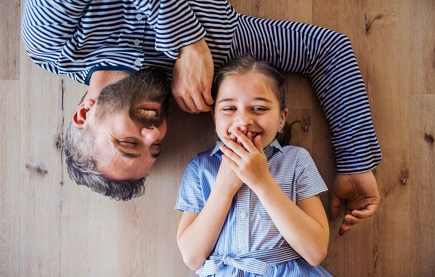 Papa und Tochter lachend auf dem Holzboden